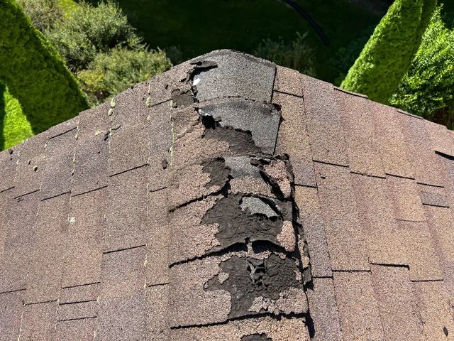 Damaged ridge cap shingles along the peak of a Vermont roof
